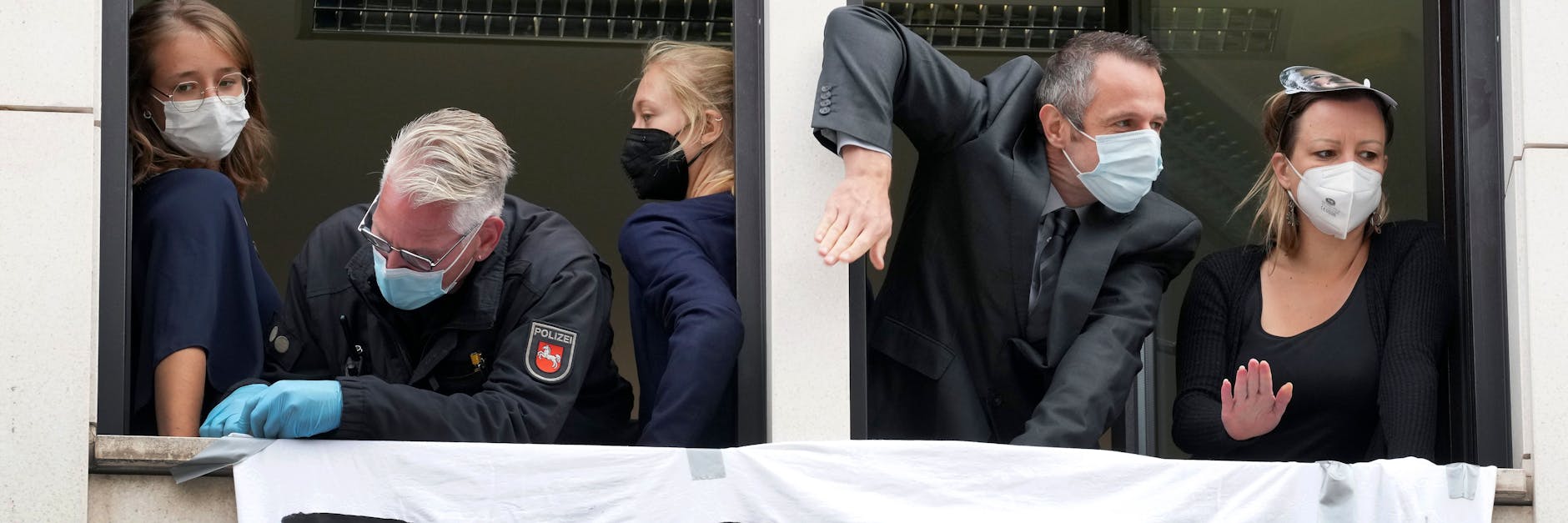 Ein Polizist versucht, die Hand einer Teilnehmerin vom Fenstersims zu befreien. Sie haftet mit Sekundenkleber an dem Gebäude.