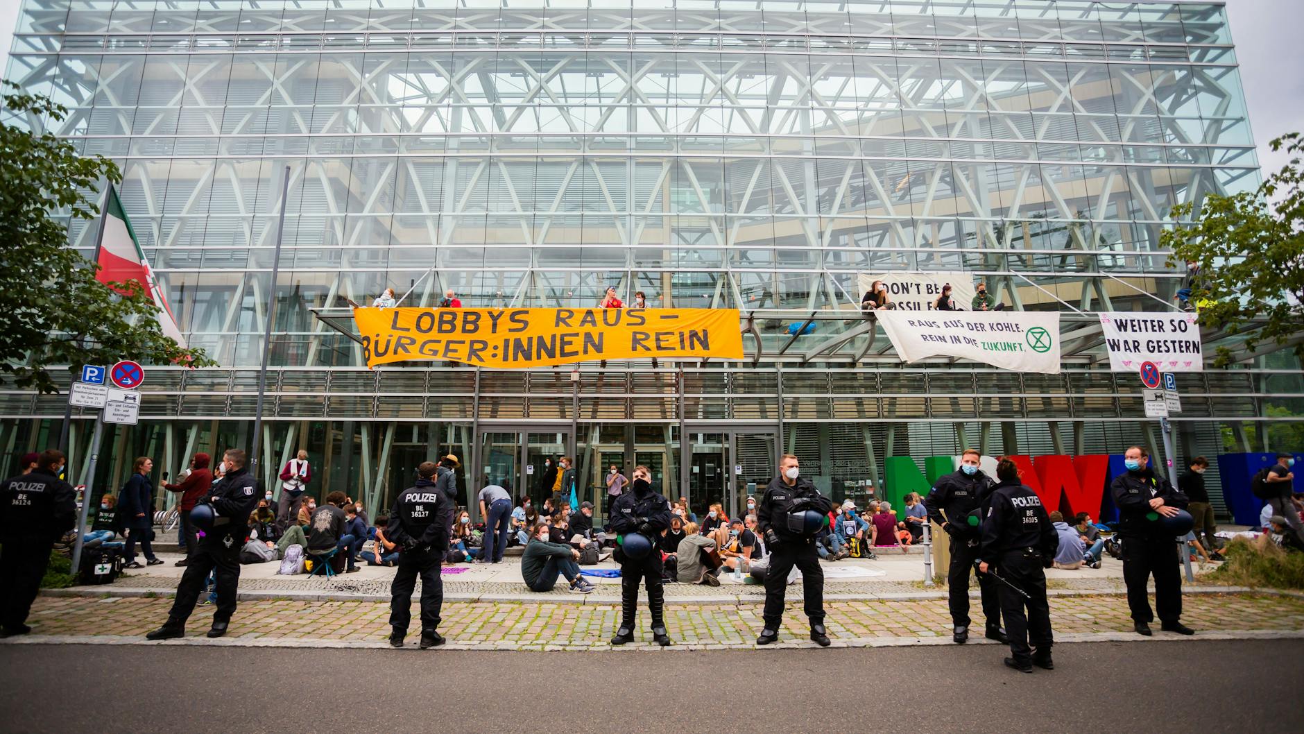 Umweltaktivisten blockieren die Landesvertretung von Nordrhein-Westfalen, wobei Polizisten davor stehen.
