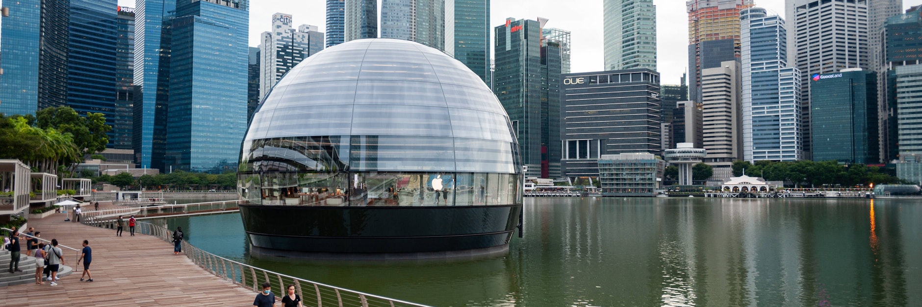 Blick auf den Apple-Flagshipstore am Ufer in Marina Bay Sands mit der Skyline des Geschaeftsviertels von Singapur im Hintergrund.