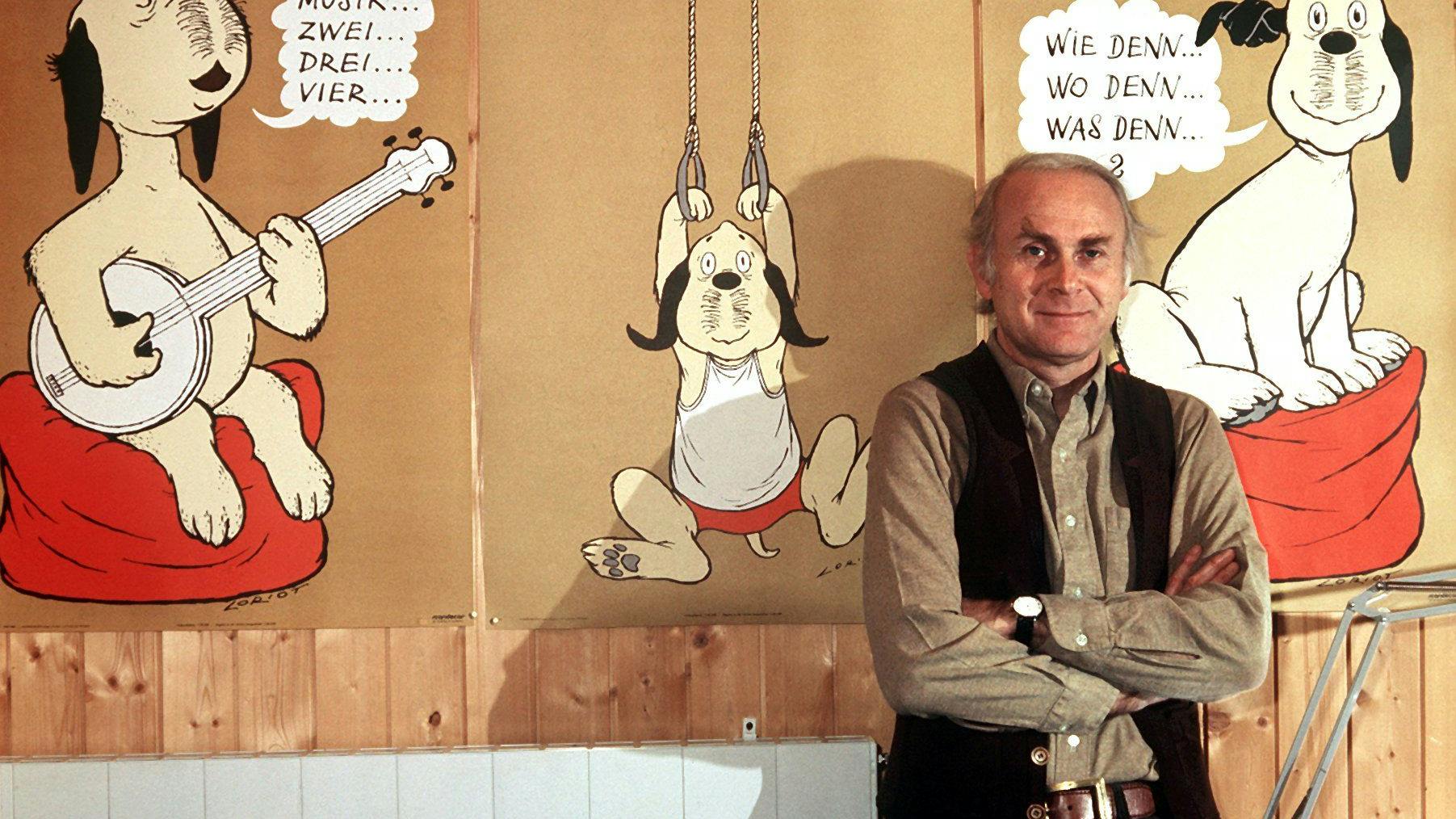 Vicco von Bülow steht in seinem Haus vor Plakaten mit dem Zeichentrickhund „Wum“.