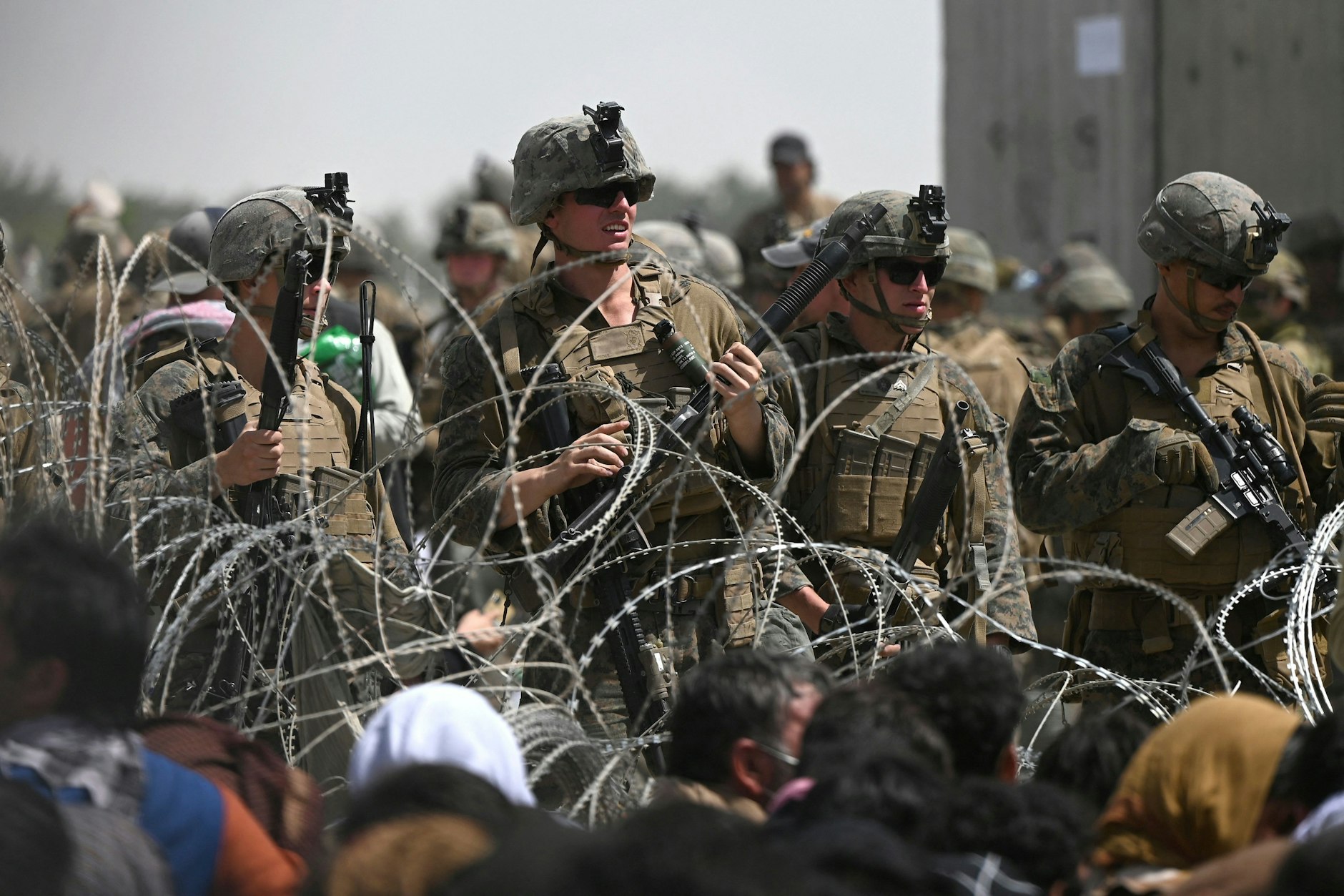 US soldiers stand guard behind barbed wire near Kabul airport, while Afghans hoping to flee the country after its military takeover by the Taliban line the roadside.