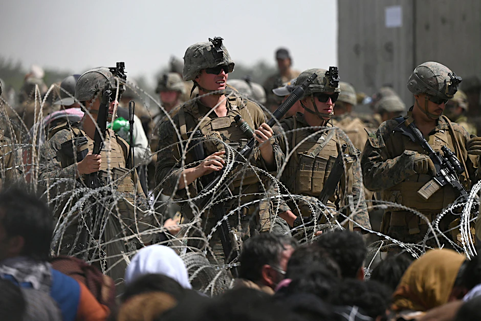 US soldiers stand guard behind barbed wire near Kabul airport, while Afghans hoping to flee the country after its military takeover by the Taliban line the roadside.
