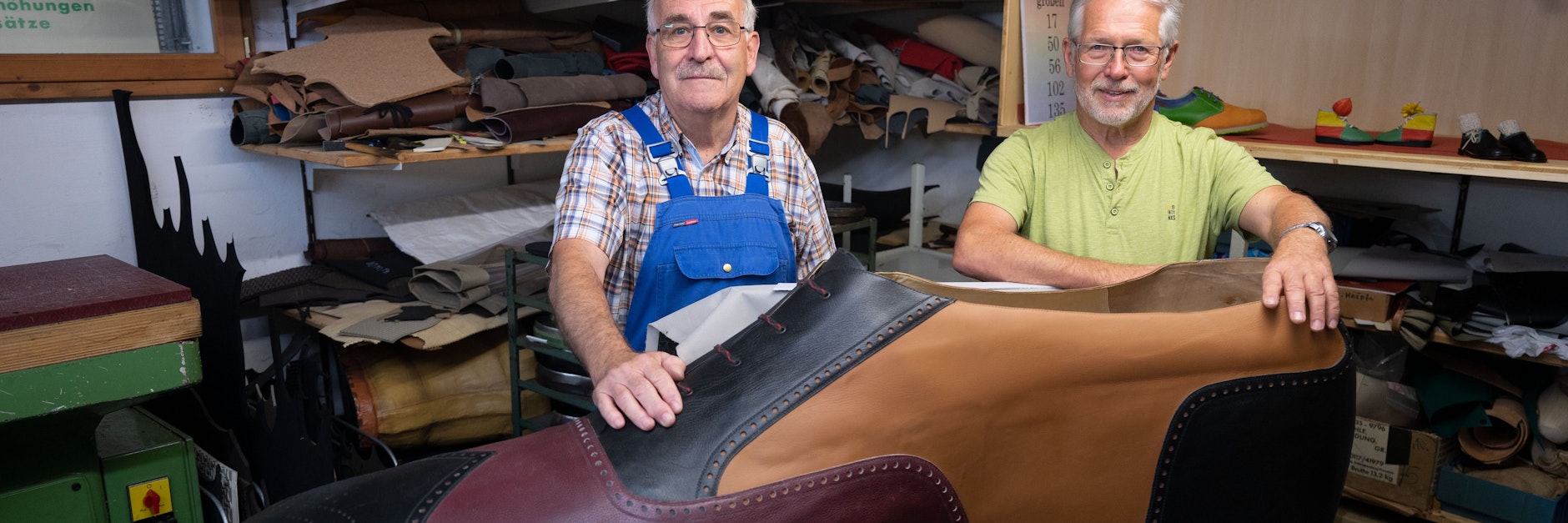 Die Schuhmachermeister Matthäus Jörg (l.) und Johannes Schunk (beide 72)  in Jörgs Werkstatt hinter dem überdimensionierten Schuh in Größe 240.