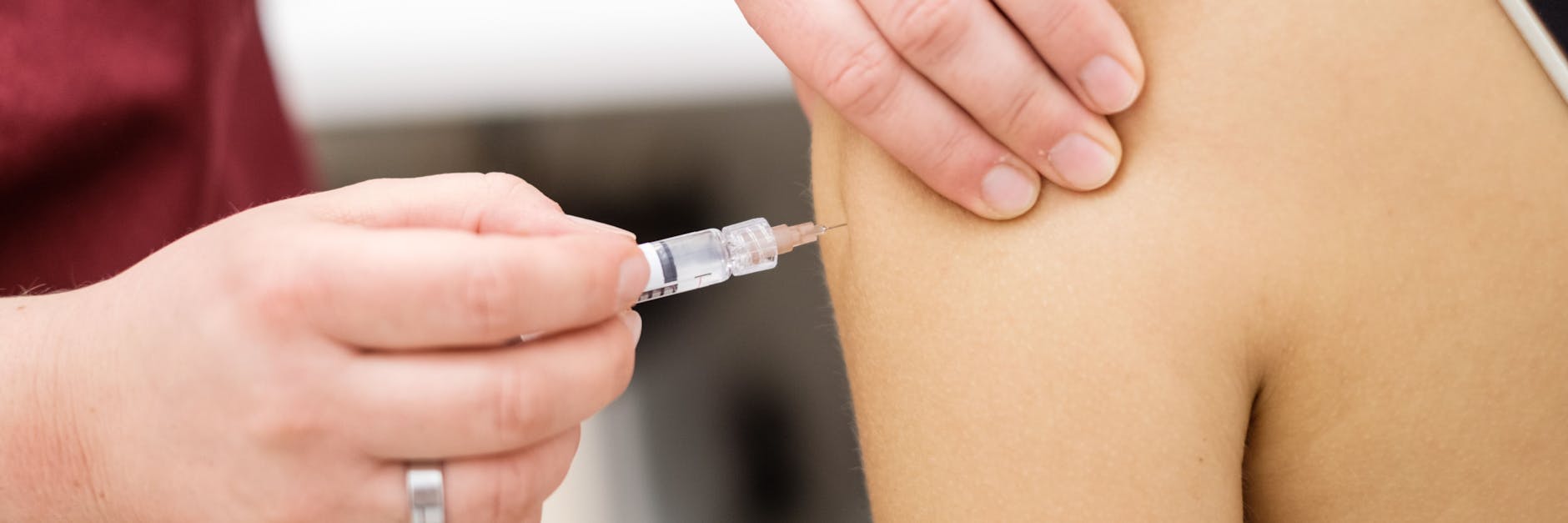 Eine Arzthelferin impft eine junge Patientin mit einer Spritze.