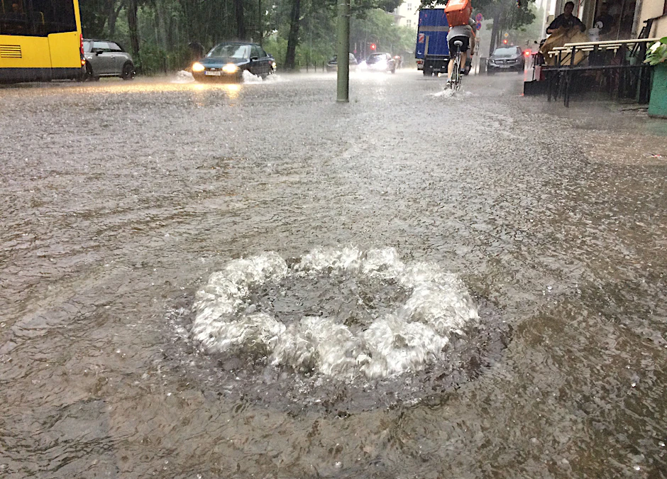 Wasser sprudelt auf einer überfluteten Straße im Stadtteil Schöneberg aus einem Gully.