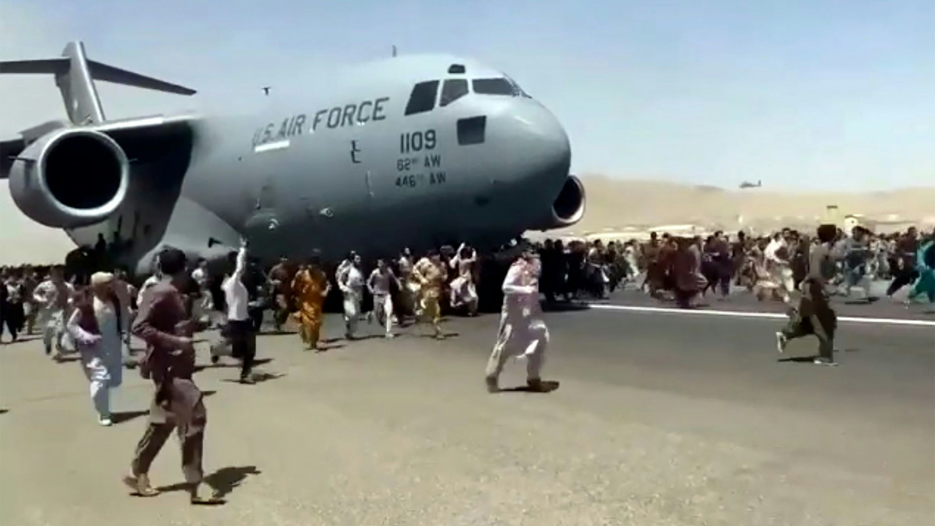 Hunderte Menschen laufen neben einer Boeing C-17 der United States Air Force, die auf dem Rollfeld des Kabul International Airport fährt.