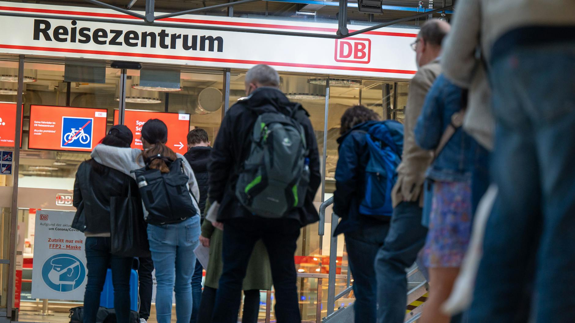 Bahnreisende warten vor einem Reisezentrum der Deutschen Bahn.
