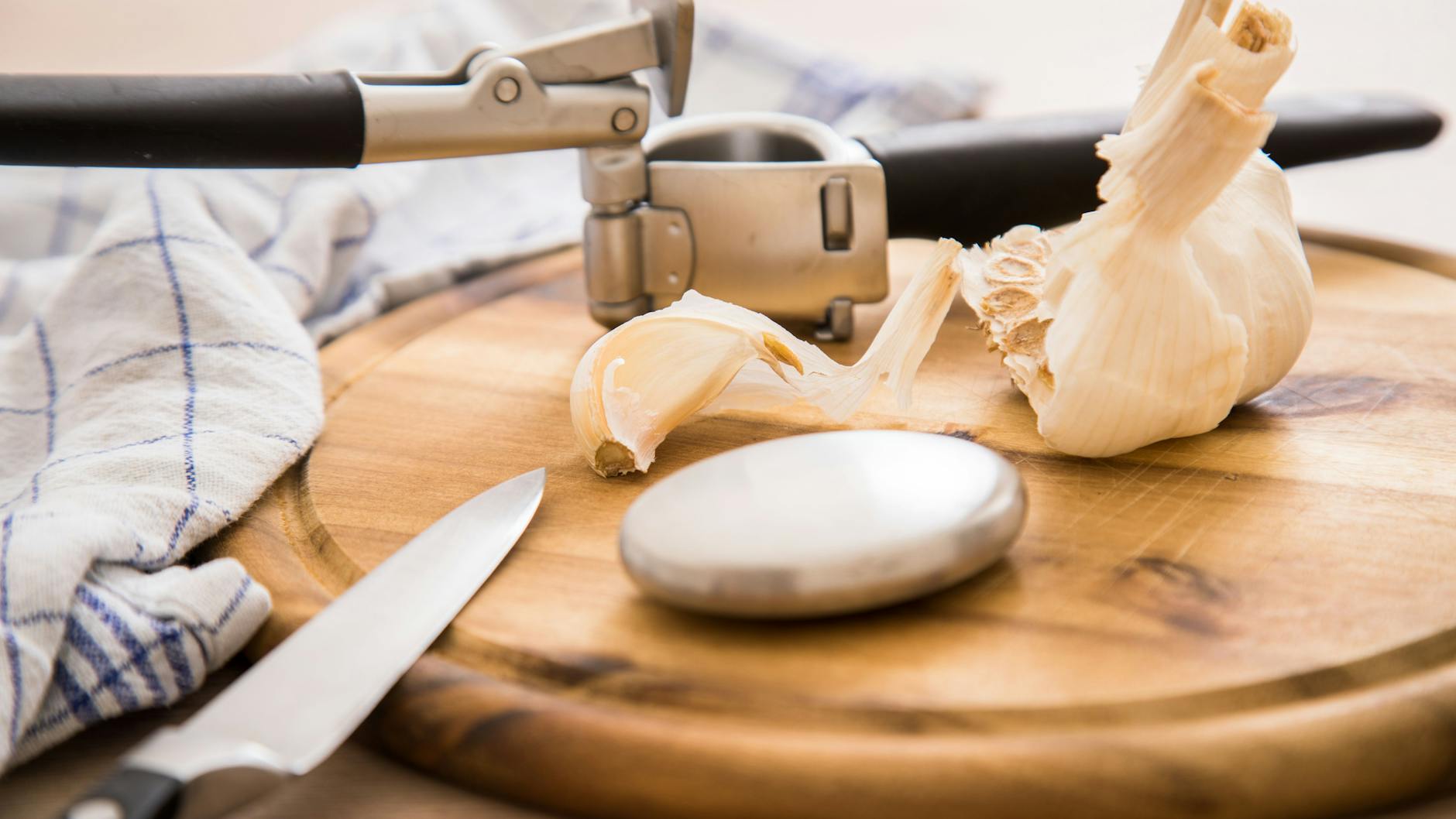 Geruchsneutralisierende Edelstahlseife liegt zusammen mit Knoblauch und einer Knoblauchpresse auf einem Holzbrett.