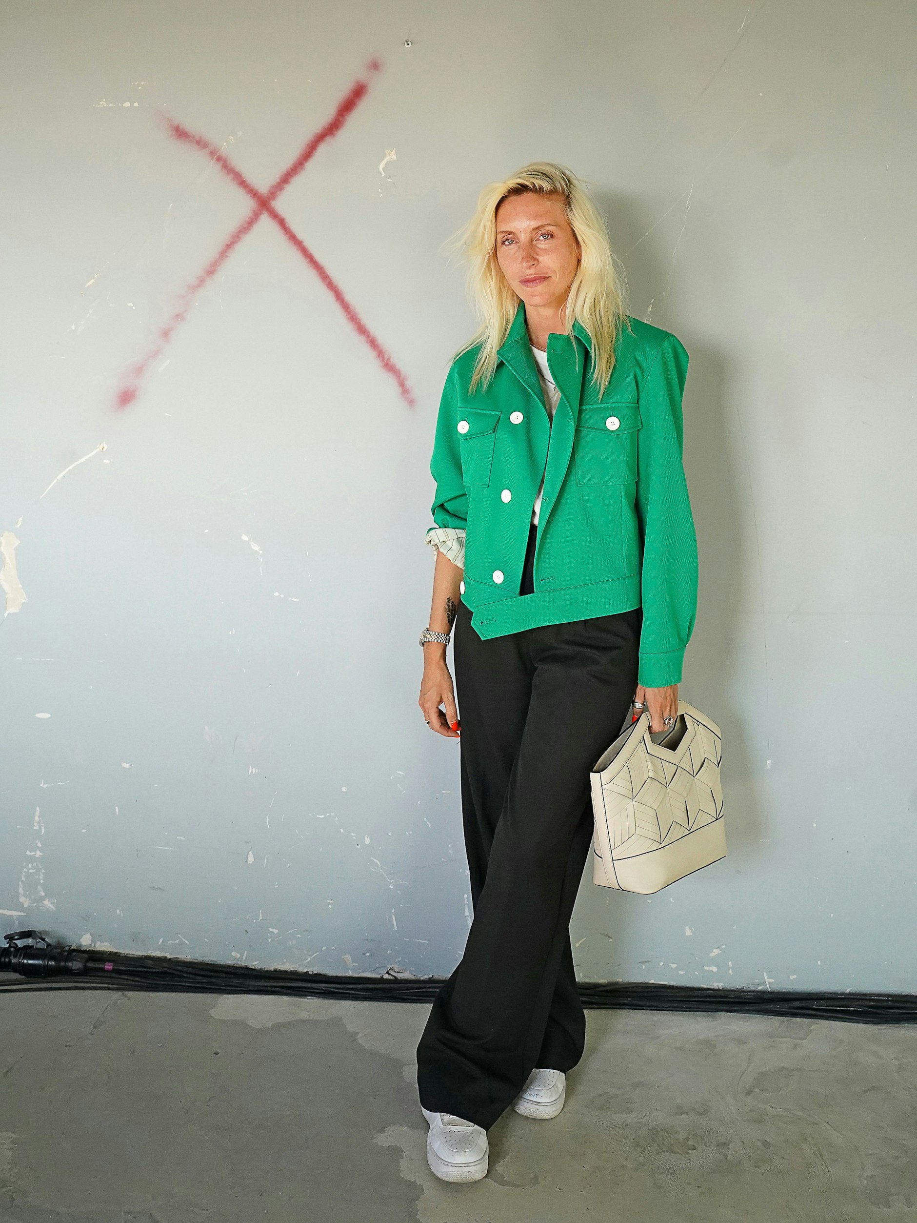 Cloudy ist Journalistin und Beraterin. Zur hellblonden Haarpracht trägt sie eine leuchtend jadegrüne Jacke der italienischen Marke Plan C, darunter ein weißes T-Shirt von Armed Angels und eine Hose von Yves Saint Laurent. Die Tasche ist von Wandler, die Halskette Vintage.