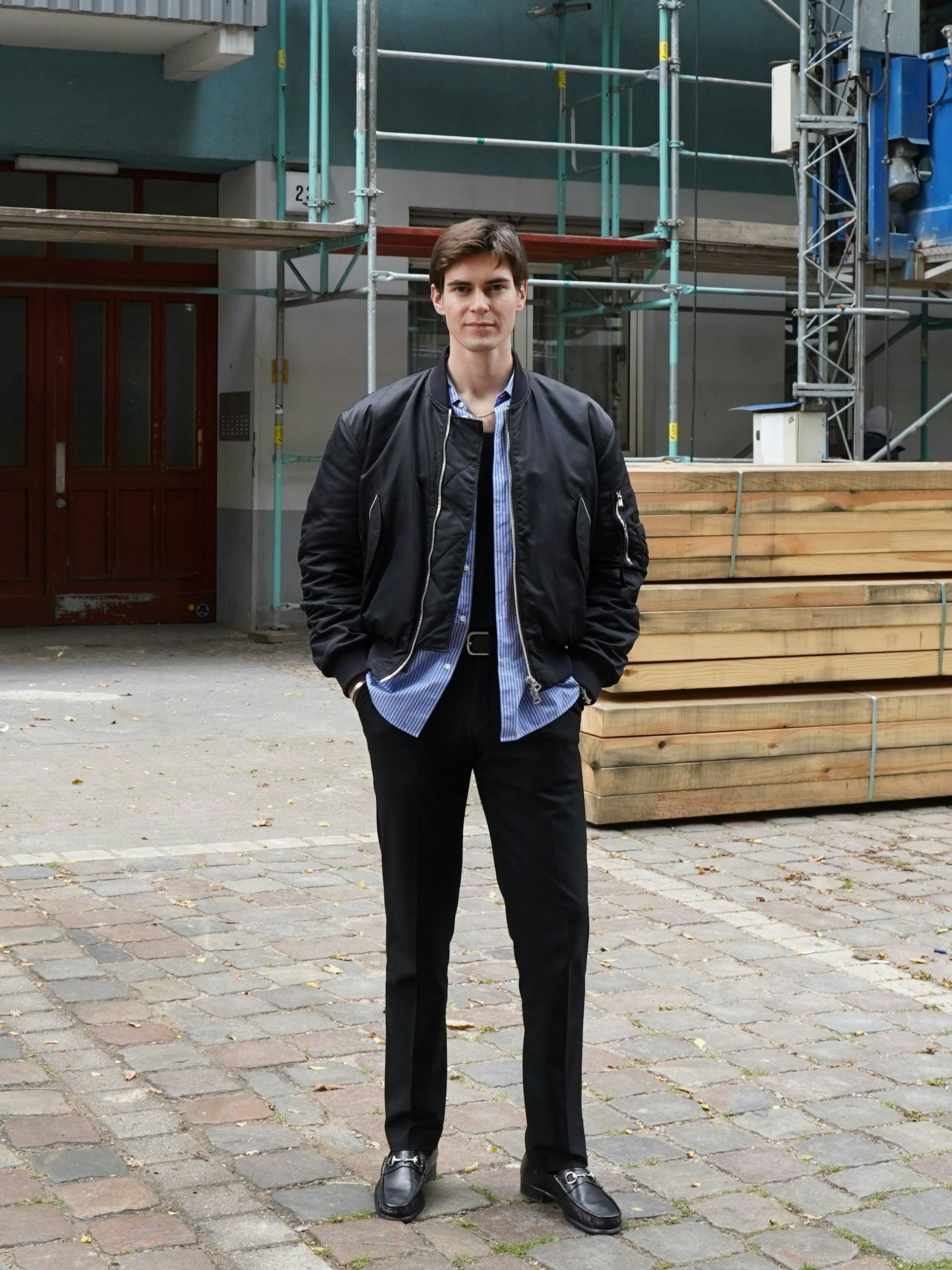 Mitch ist Brand-Manager bei Swype, der Firma von Ebru. Er wohnt eigentlich in Mitte, liebt aber das Büro in dieser Straße und findet die Leute hier in Wedding „echt“, im Vergleich zu anderswo. Zur Bomberjacke von Acne Studios trägt er ein blau-weiß gestreiftes Hemd, ein schwarzes Shirt und eine Hose, alles von Uniqlo. Die Kette hat Mitch vom Flohmarkt auf dem Arkonaplatz.