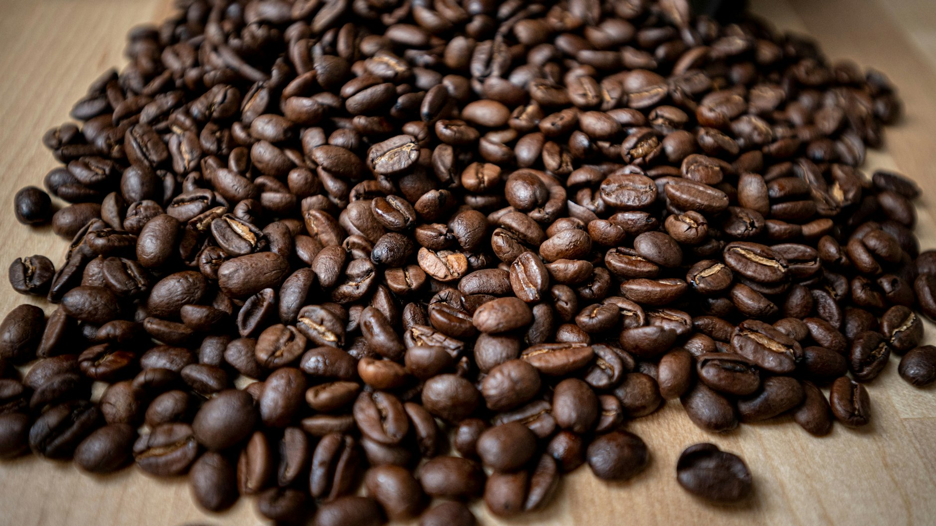 Geröstete Kaffeebohnen liegen auf einem Tisch. Kaffee ist der Deutschen liebstes Getränk.