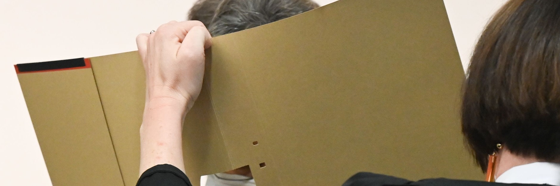 Die angeklagte 60-jährige Frau im Gerichtssaal des Landgerichts mit einem Aktenordner vorm Gesicht.