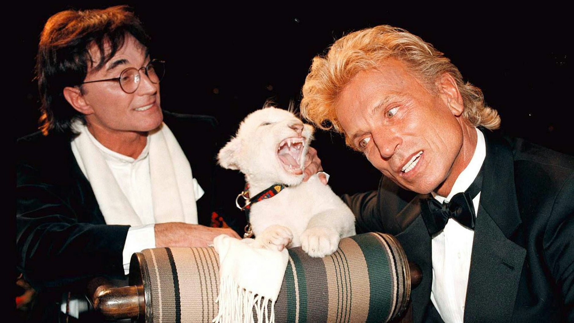 Siegfried Fischbacher und Roy Horn posieren in Siegfrieds Heimatstadt Rosenheim mit einem kleinen, weißen Löwen.