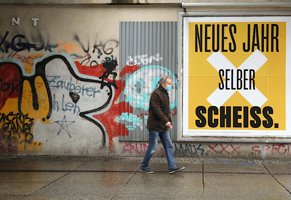 Ein Mann mit Maske spaziert in Berlin an einer beklebten Hauswand vorbei.&nbsp;