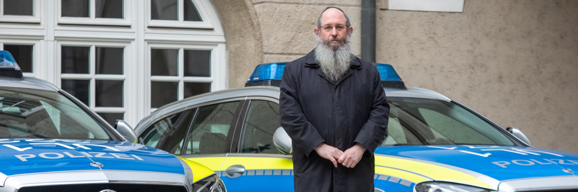 Rabbiner Shneur Trebnik steht im Ulmer Polizeipräsidium zwischen zwei Streifenwagen.&nbsp;