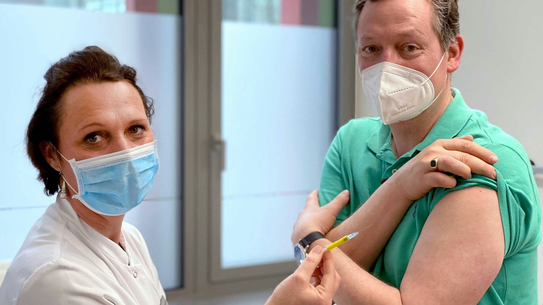 Arzt und Wissenschaftsjournalist Eckart von Hirschhausen steht neben Studienleiterin Professor Clara Lehmann (Uniklinik Köln), die eine Spritze in der Hand hält. Hirschhausen hat für eine TV-Doku an einer Impfstudie in Köln teilgenommen. 