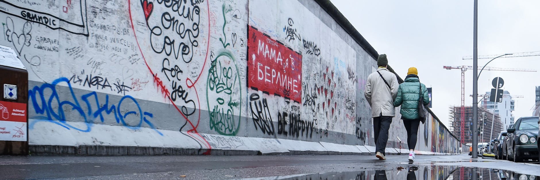 Zwei Personen gehen an der Berliner Mauer entlang. 