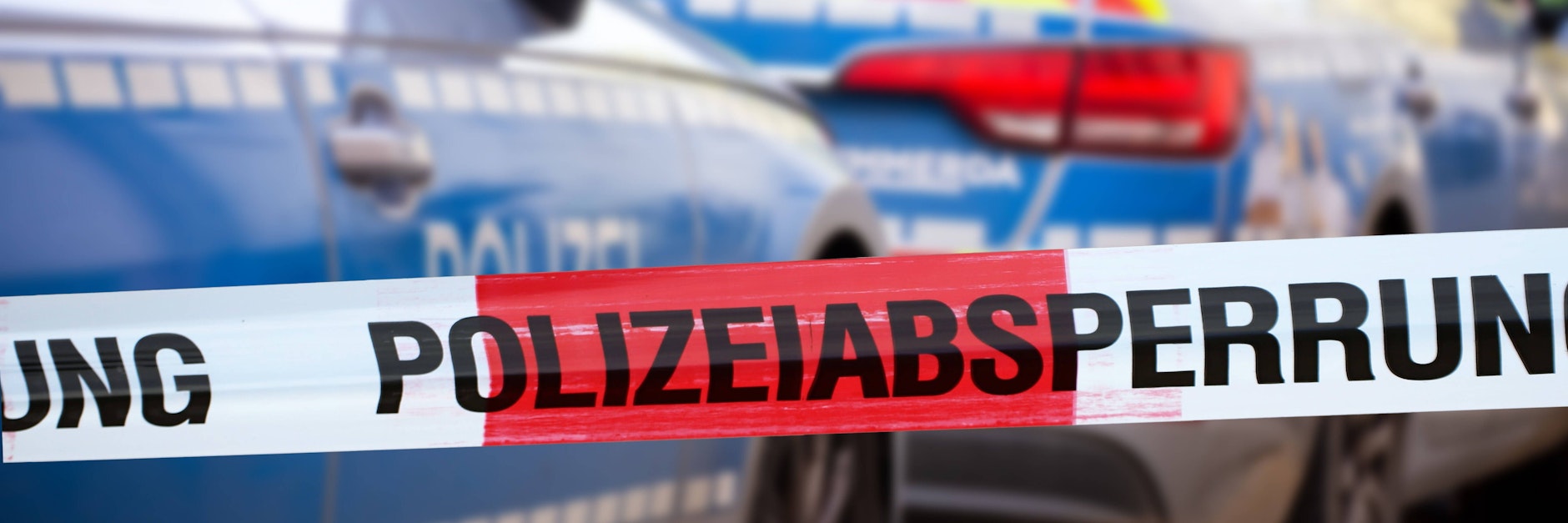 Eine Polizeiabsperrung mit Polizeiauto im Hintergrund
