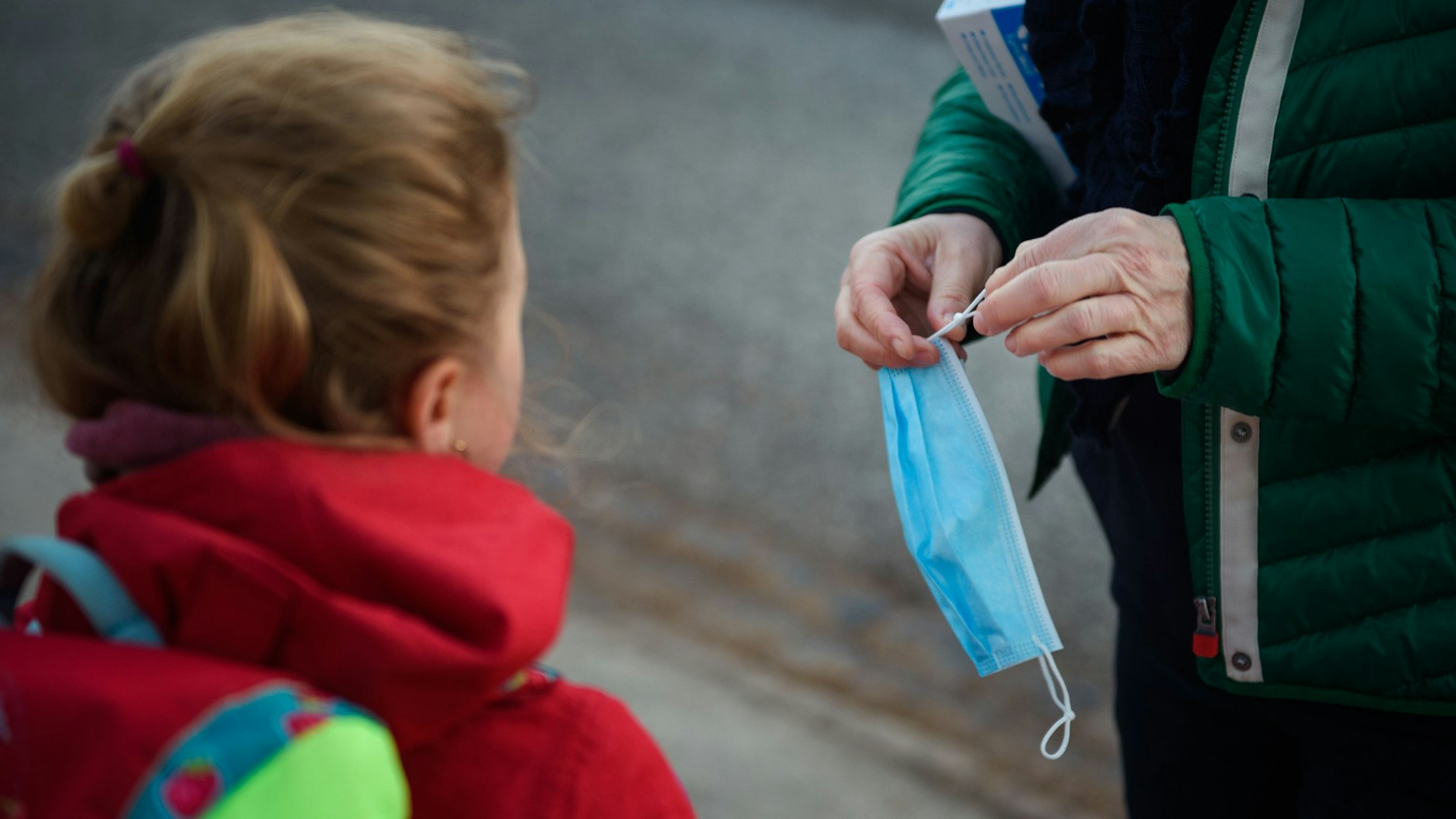 Eine Erwachsene kürzt für eine Grundschülerin ihre Maske, damit sie besser hält. Seit Montag ist die Maskenpflicht an Berliner Grundschulen weggefallen.