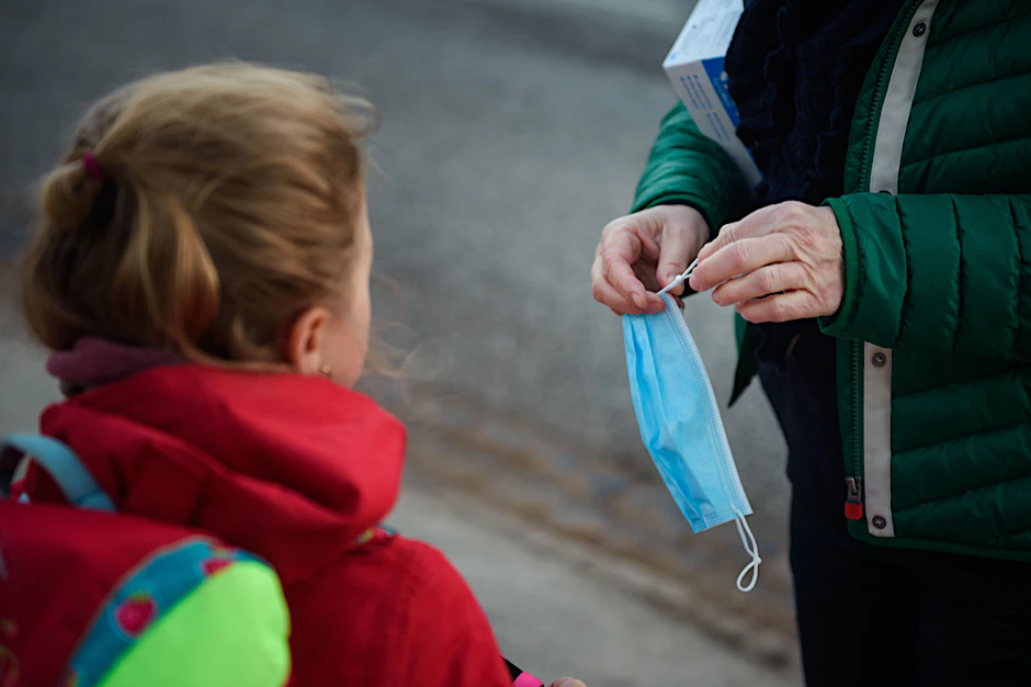 Eine Erwachsene kürzt für eine Grundschülerin ihre Maske, damit sie besser hält. Seit Montag ist die Maskenpflicht an Berliner Grundschulen weggefallen.