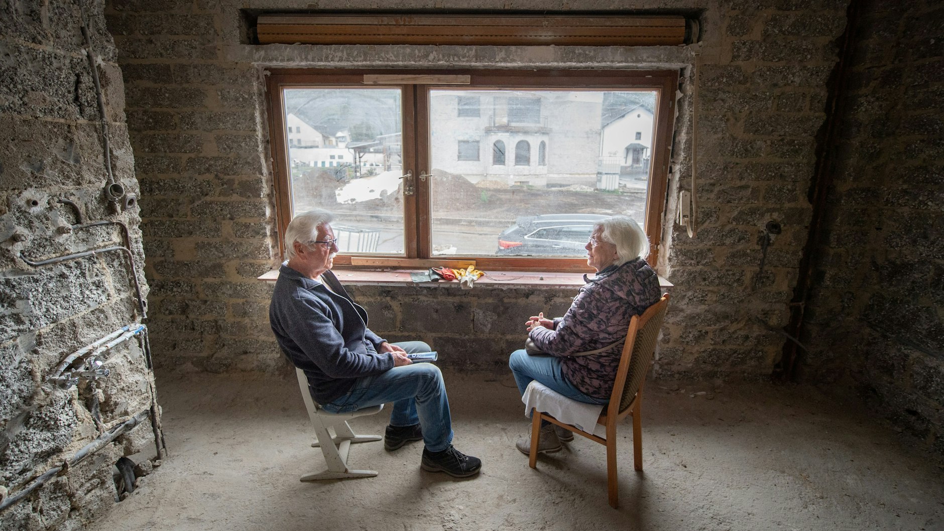 Elfriede und Gerd Gasper sitzen im völlig entkernten, ehemaligen Wohnzimmer ihres von der Flut zerstörten Hauses in Altenahr, von wo aus sie die Trümmer des Ortes sehen können.