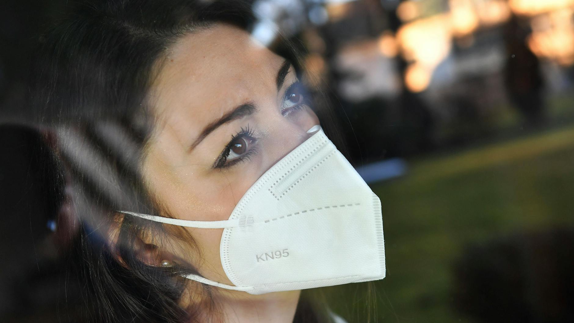 Eine Frau mit FFP2-Maske schaut bekümmert aus einem Fenster. Corona und die politischen Maßnahmen belasten zusehends die Menschen aller Altersgruppen (Symbolbild).