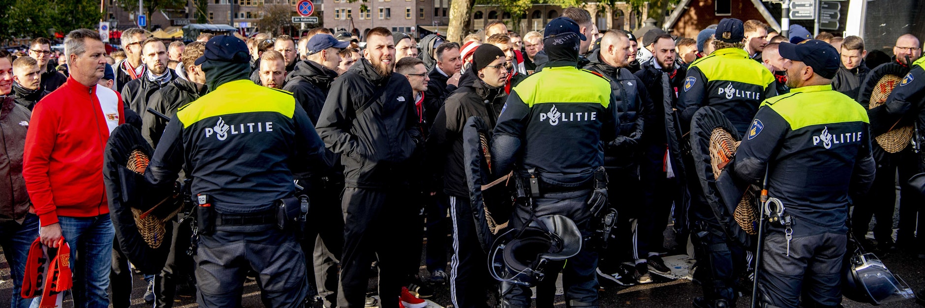 Fans des 1. FC Union Berlin vor dem Spiel in Rotterdam am Alten Hafen warten hinter einer Polizeikette darauf, dass sie zum Stadion von Feyenoord können.