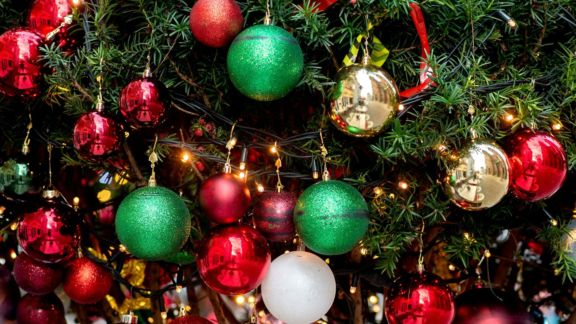 Ein Weihnachtsbaum ist mit zahlreichen Christbaumkugeln und Lichterketten weihnachtlich geschmückt. 