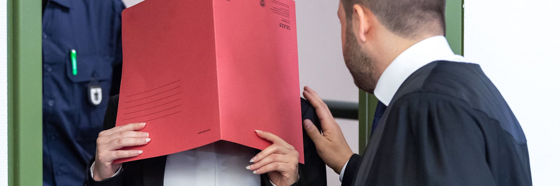 Die Angeklagte Jennifer W., die sich der Terrormiliz Islamischer Staat (IS) im Irak angeschlossen haben soll, hält sich beim Betreten des Gerichtssaals einen roten Aktendeckel vors Gesicht.