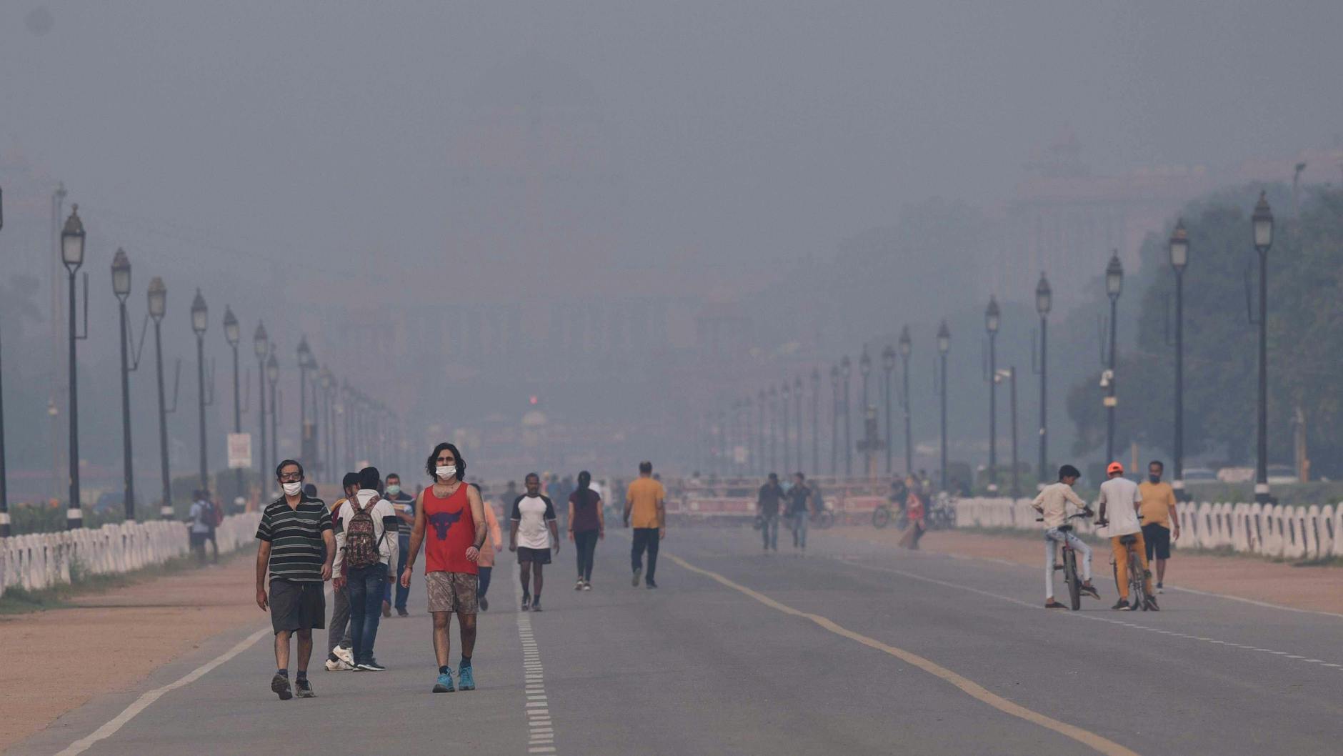 Neu Delhi: Menschen gehen im Smog auf einer Straße. Indien will bis 2070 Klimaneutralität erreichen.