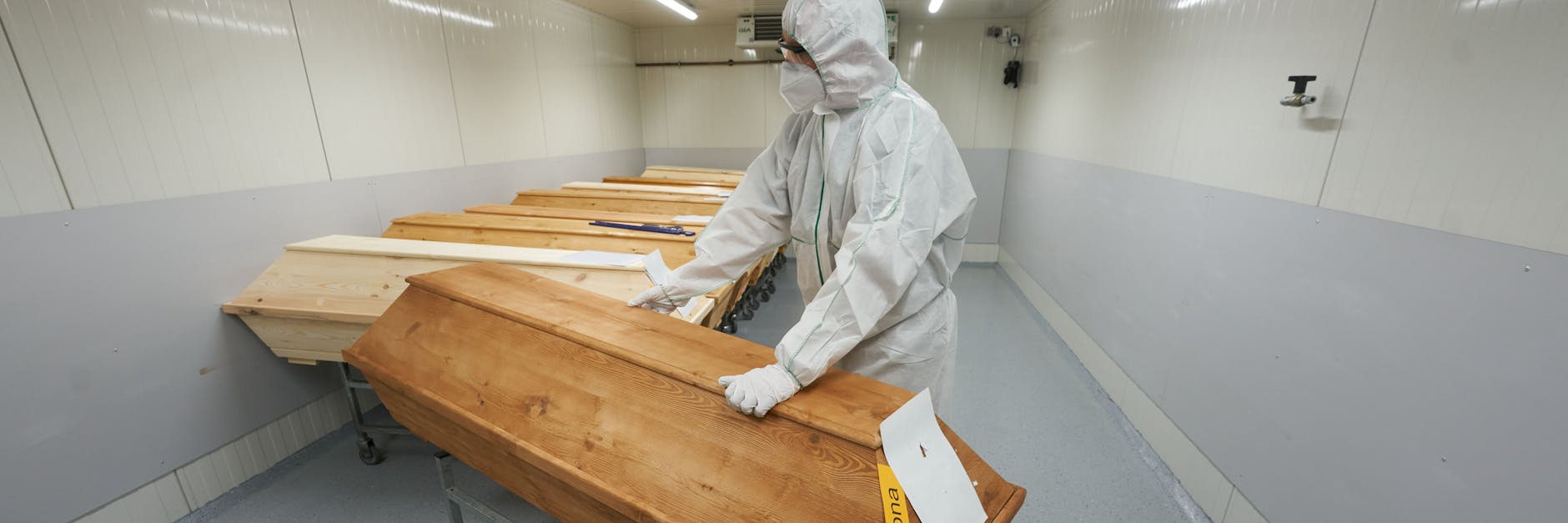 Ein Krematoriums-Mitarbeiter in Schutzkleidung schiebt einen Sarg mit einem Covid-19-Opfer.