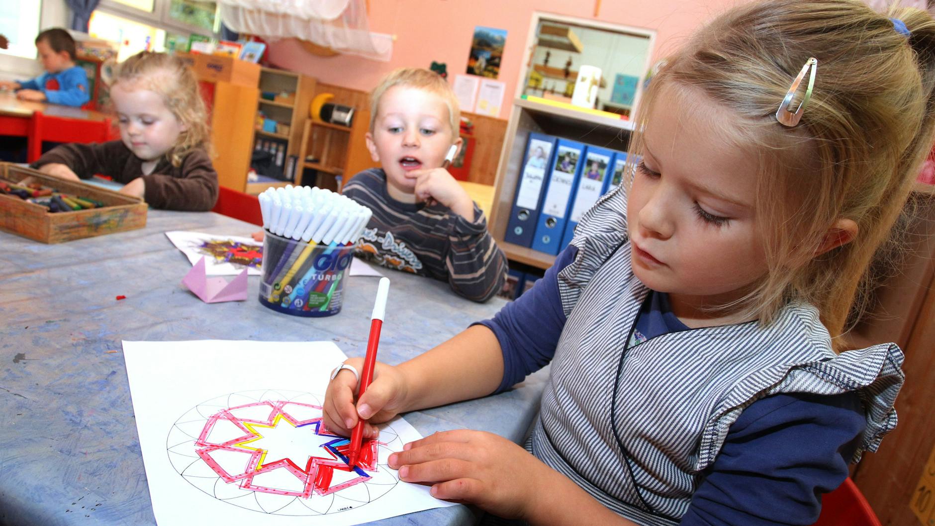 Ein Mädchen malt ein Bild. Die Zahl der Kinder, die noch ein Jahr länger in der Kita bleiben, steigt. Die Gründe dafür sind neben Corona unterschiedlich.