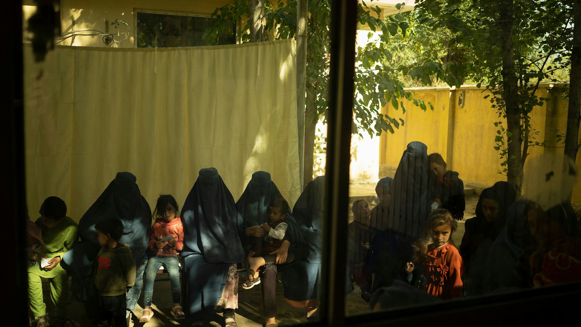 Frauen, in Burkas eingemummelt, warten mit ihren Kindern vor dem Krankenhaus auf Behandlung.