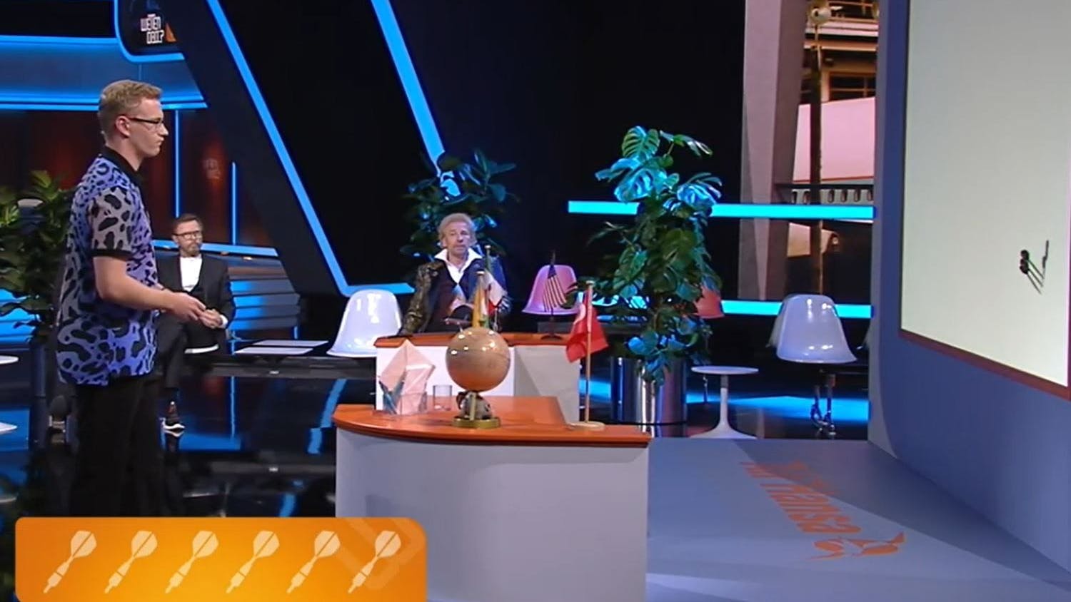 Leon wirft mit Dartpfeilen auf eine Karte, die man nicht sieht.