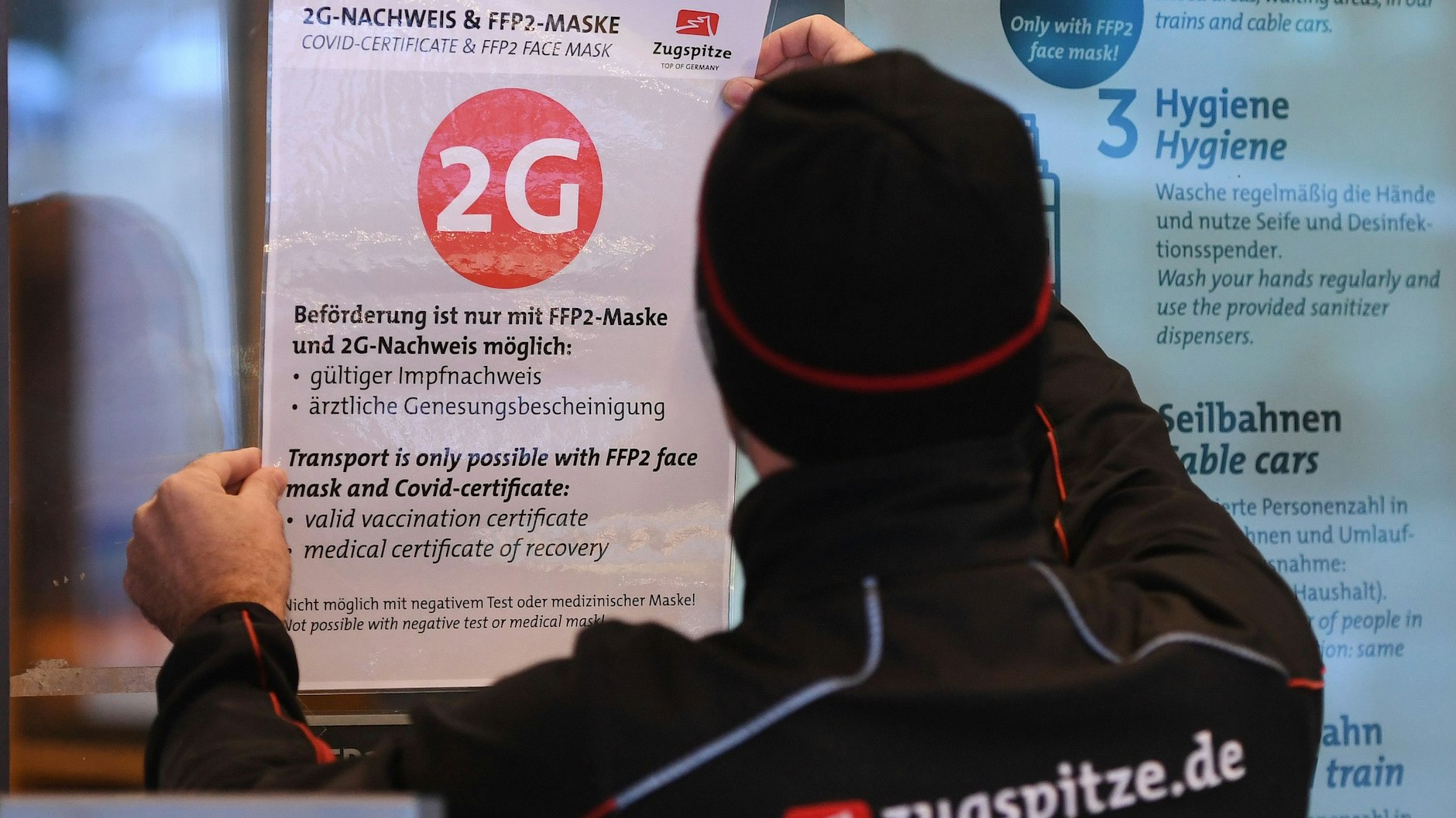 Ein Mitarbeiter der Zugspitzbahn klebt einen 2G-Hinweis an die Eingangstür der Talstation. Für viele Bereiche gilt ab Dienstag die 2G-Regel.