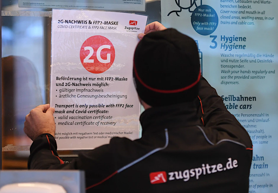 Ein Mitarbeiter der Zugspitzbahn klebt einen 2G-Hinweis an die Eingangstür der Talstation. Für viele Bereiche gilt ab Dienstag die 2G-Regel.