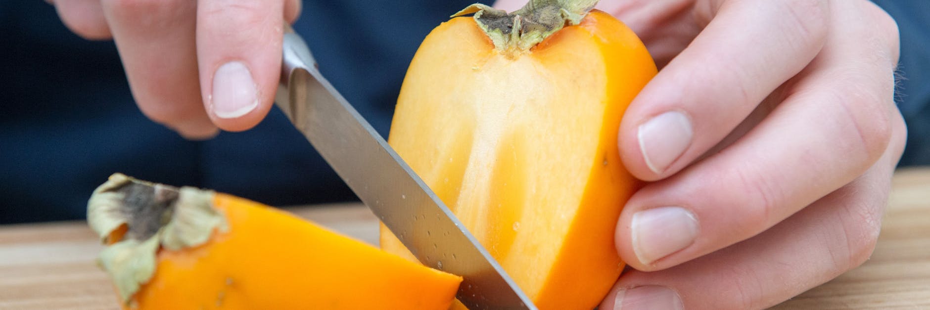 Mit einem scharfen Messer wird die Kaki längs halbiert. Danach wird der Stielansatz herausgeschnitten.