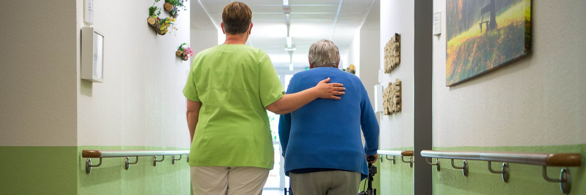 Eine Pflegefachkraft geht mit einer Bewohnerin durch das Seniorenheim.