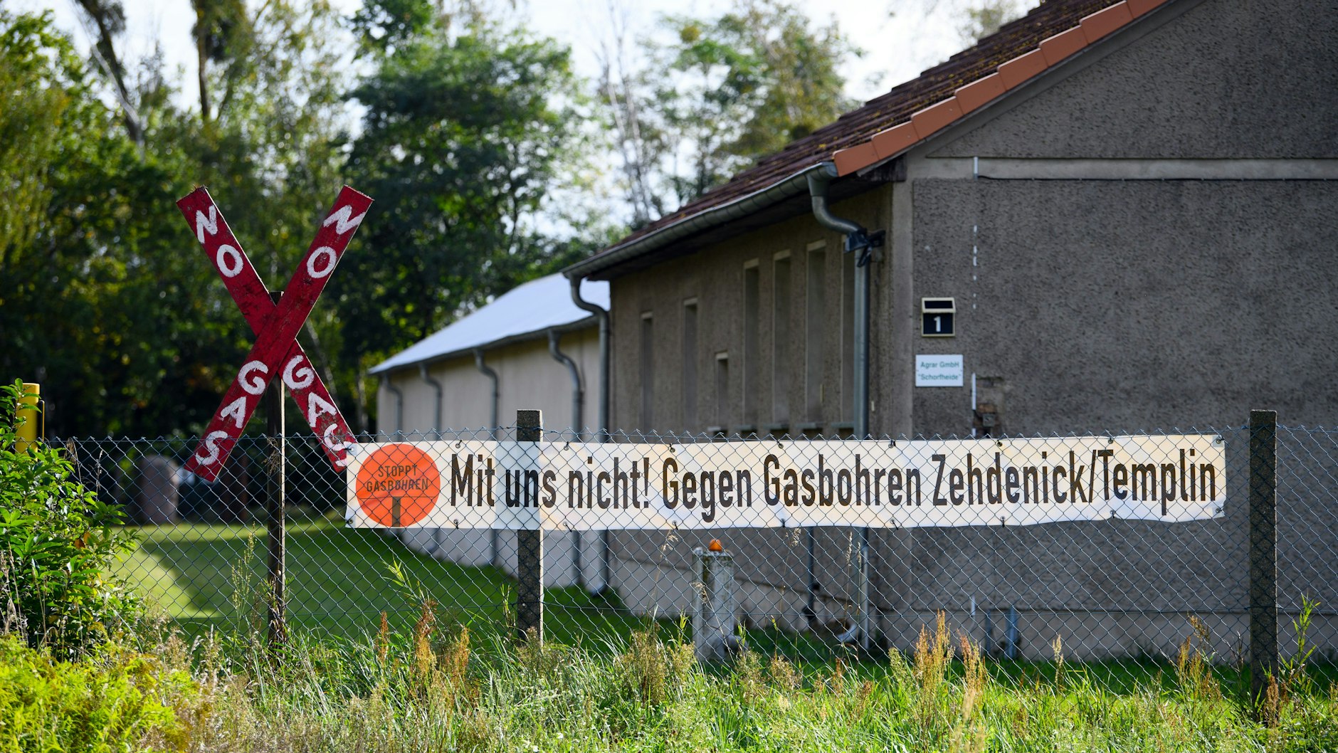 Ein Transparent mit der Aufschrift „Mit uns nicht! Gegen Gasbohren Zehdenick/Templin“ hängt an einem Zaun neben einem roten Holzkreuz mit der Aufschrift „No Gas“