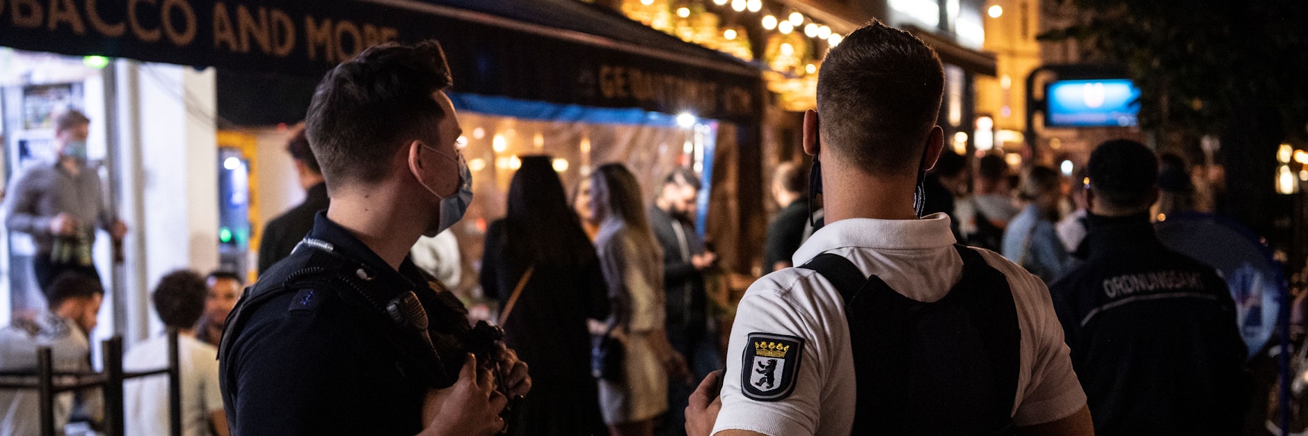 Ein Polizeibeamter und ein Mitarbeiter des Ordnungsamtes stehen vor einem Lokal in Berlin.