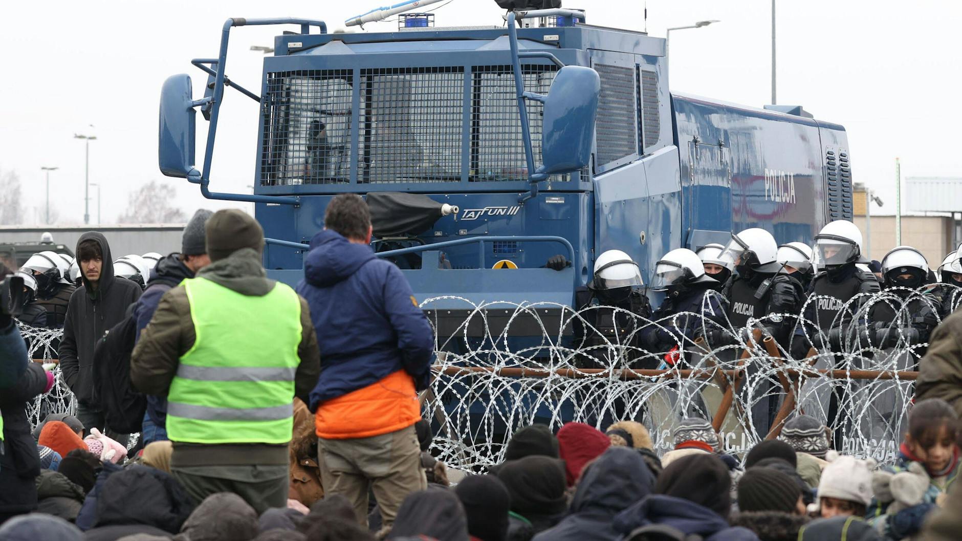 Migranten stehen an der belarussischen Grenze polnischen Polizisten gegenüber.