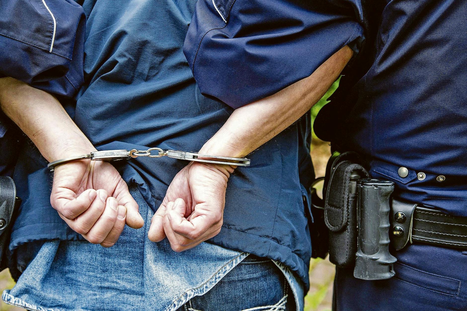 Ein Polizist führt einen Verdächtigen in Handschellen ab (Symbolbild).