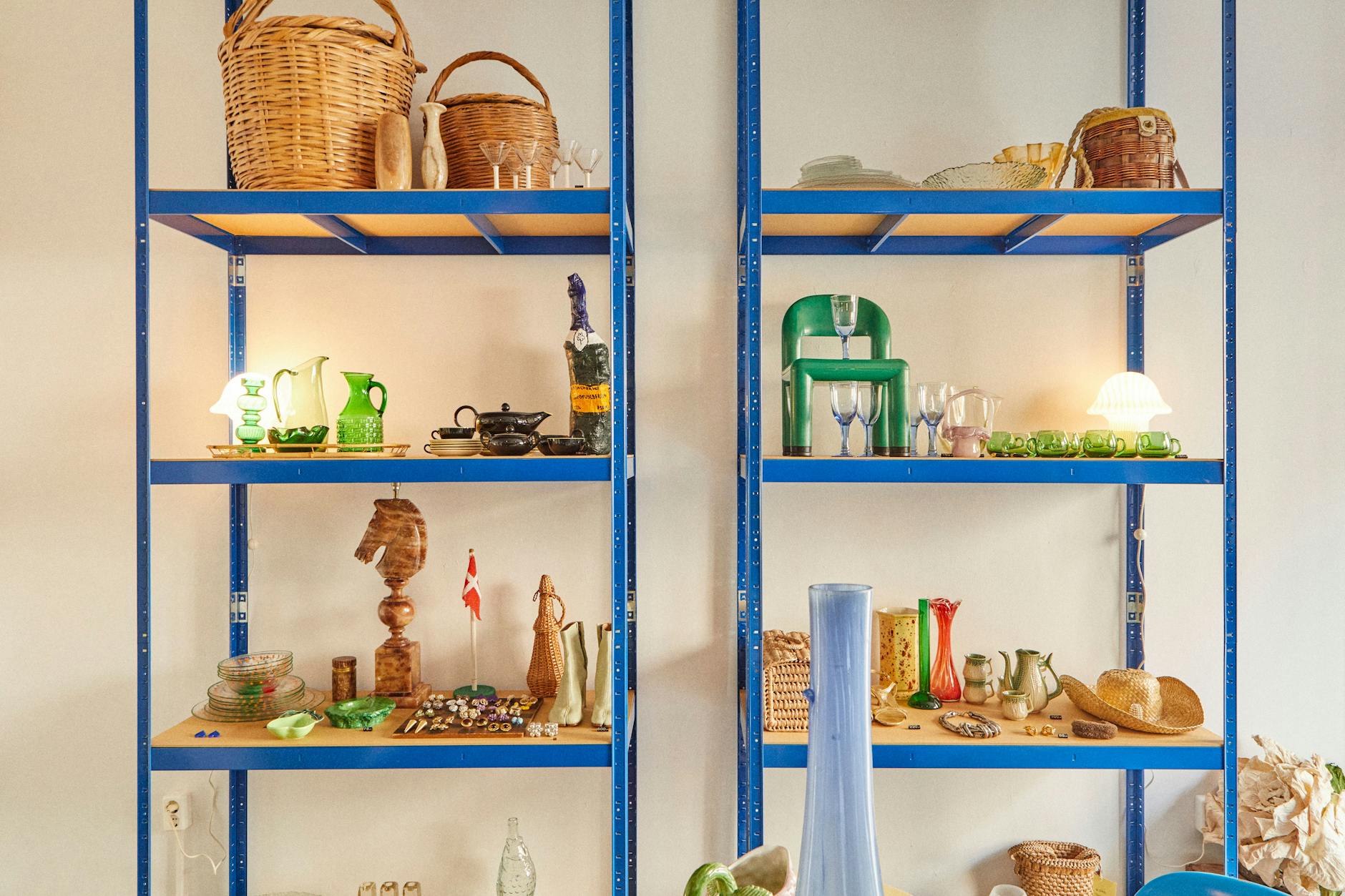 Auf dem blauen Metallregal: flaschengrüne Vasen nebst Margielas Tabi-Boots, Teeservice, Miu-Miu-Sandalen.