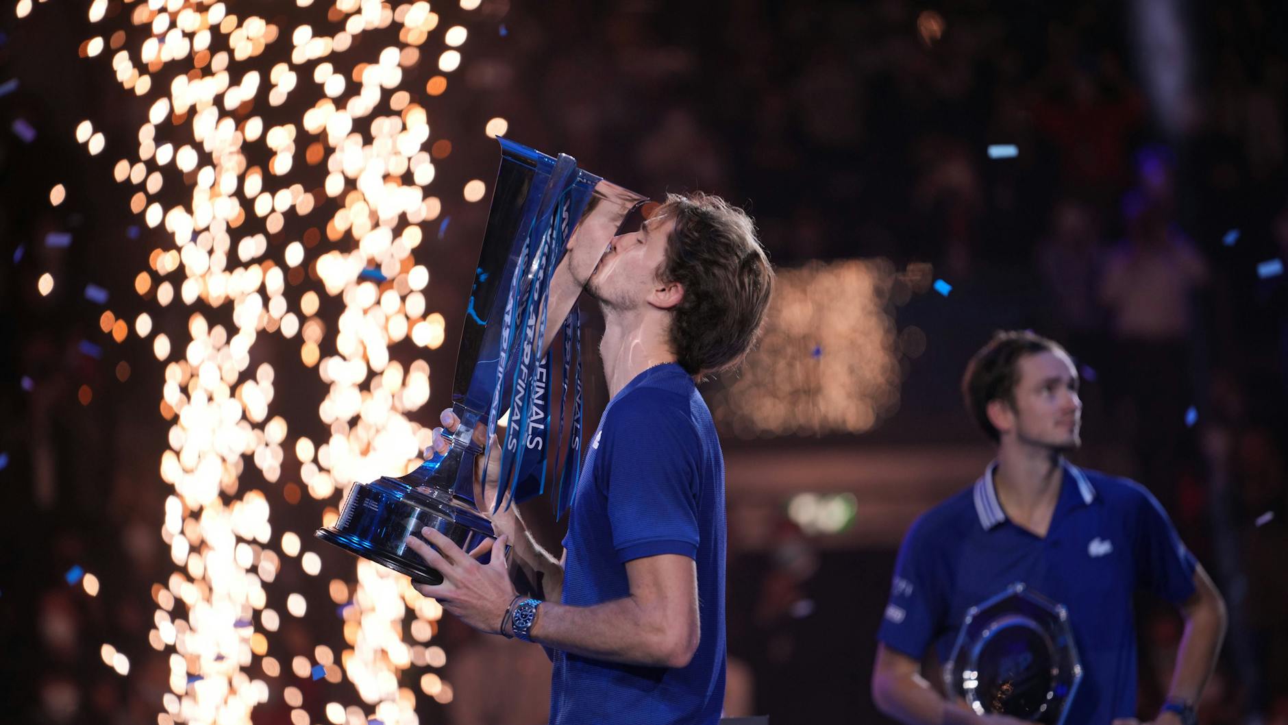 Ein Feuerwerk und Endspielgegner Daniil Medwedew im Hintergrund: Alexander Zverev küsst den silbernen Siegerpokal bei den ATP Finals.