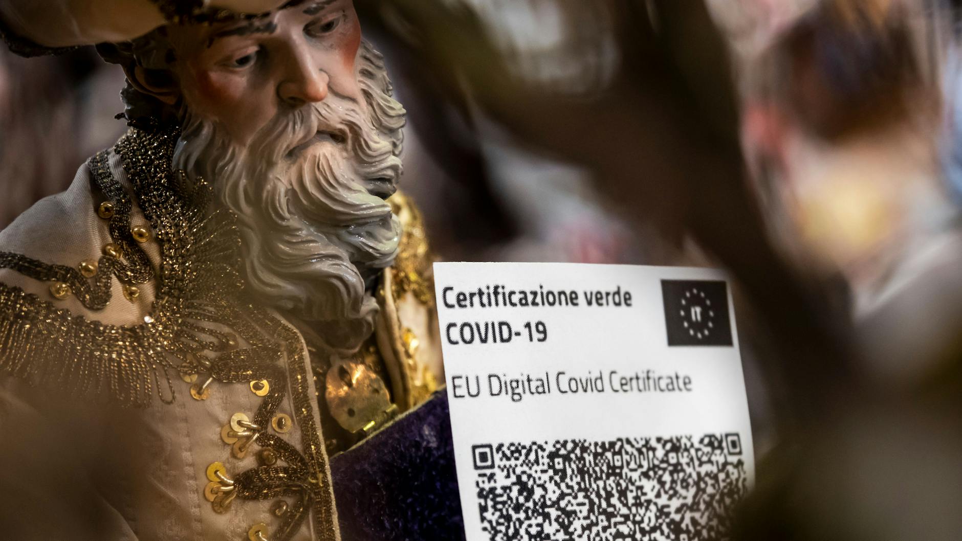 Eine Figur einer Weihnachtskrippe hält ein Coronavirus-Impfzertifikat in den Händen. Der „Grüne Pass“ soll nur noch neun Monate gültig sein (Symbolbild).