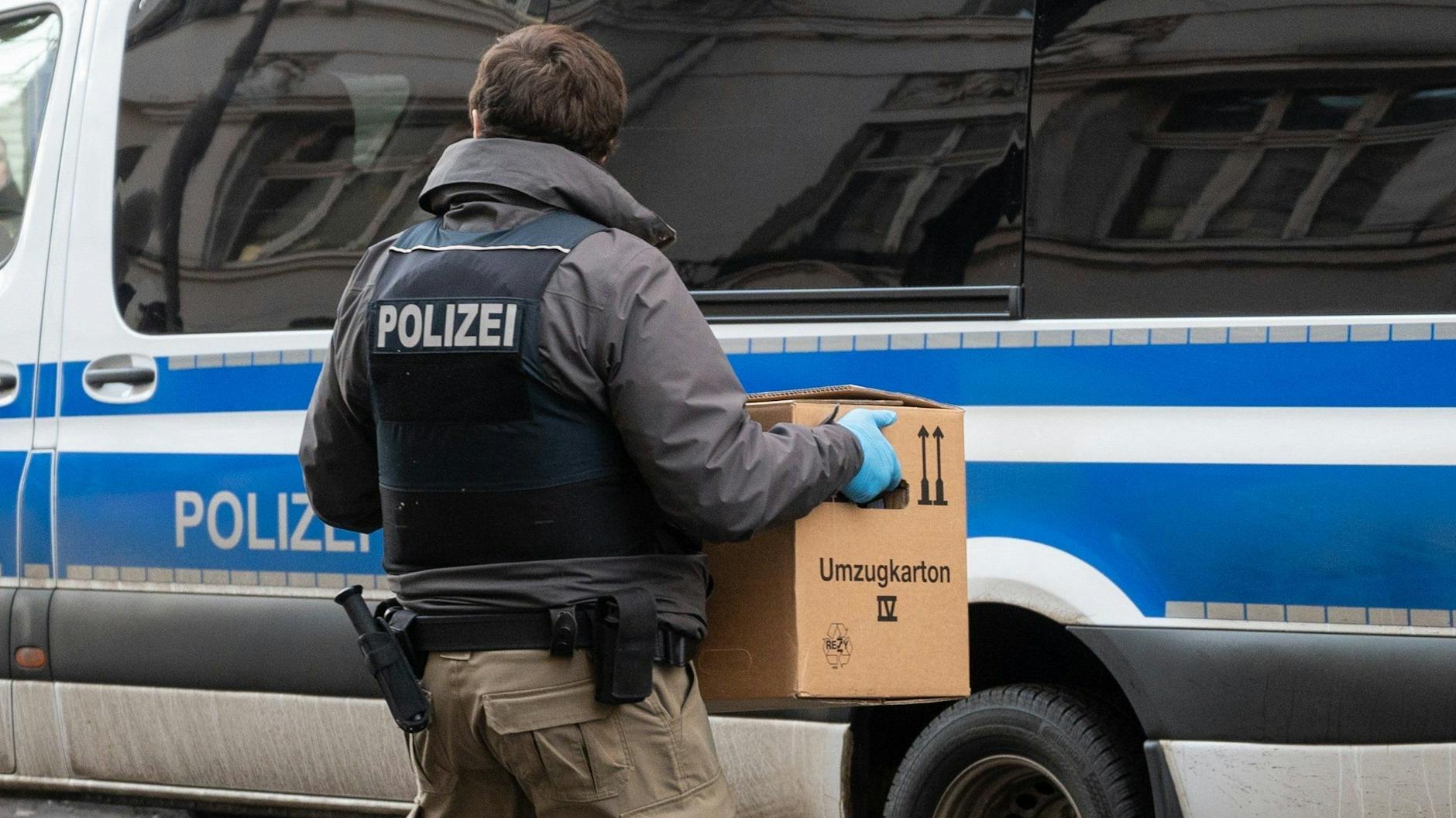 Ein Polizist trägt bei einer Razzia in Berlin eine Kiste mit Beweismitteln zum Einsatzwagen.