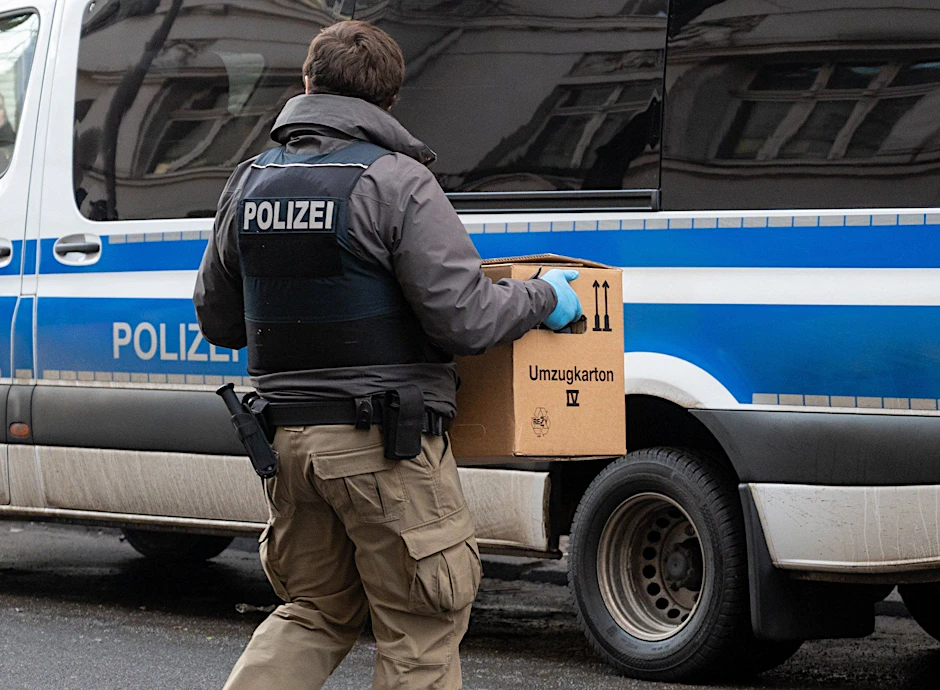 Ein Polizist trägt bei einer Razzia in Berlin eine Kiste mit Beweismitteln zum Einsatzwagen.