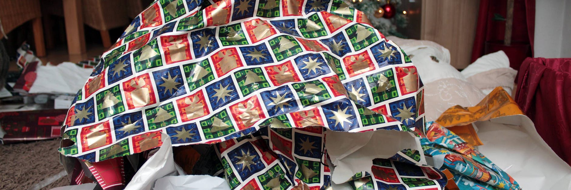 Vor einem Weihnachtsbaum türmt sich ein Berg mit Geschenkpapier. Das muss nicht sein.