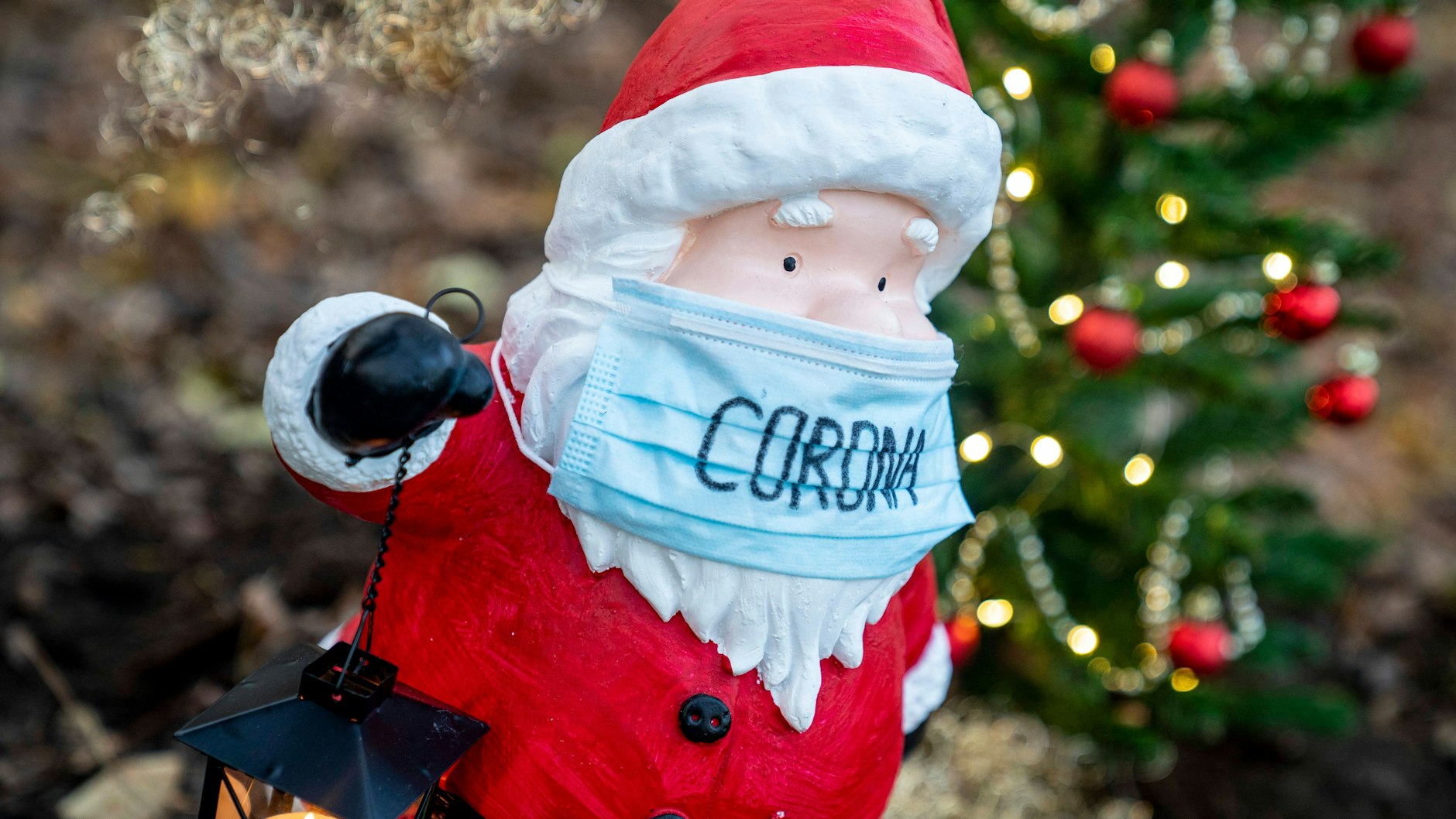 Eine Weihnachtsmannfigur mit Corona-Maske steht vor einem Weihnachtsbaum (Symbolbild). Die Festtage stehen dieses Jahr wieder im Zeichen der Pandemie.