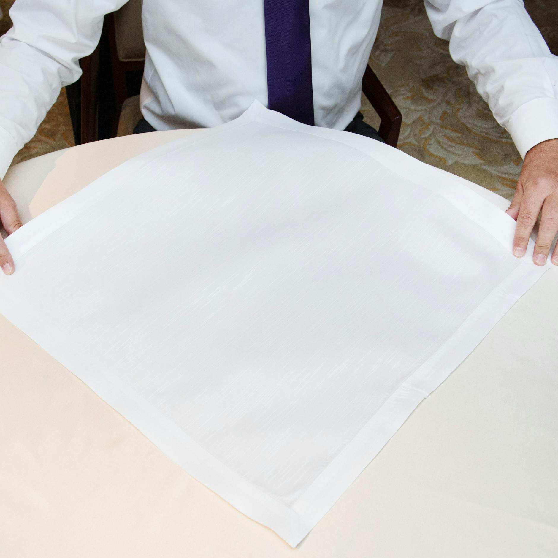 Schritt 1: Die Serviette als Raute auf den Tisch legen. Nun die unterste Ecke auf die obere falten.